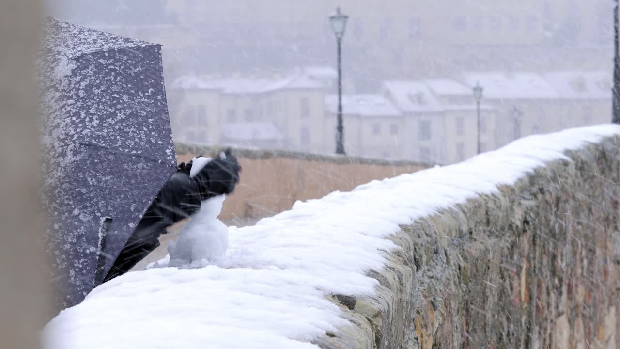 우산으로 덮인 눈보라 동안 돌담에 눈사람 만들기