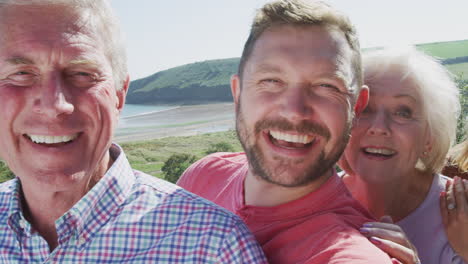 Portrait-Of-Senior-Couple-With-Adult-Offspring-Posing-For-Selfie-On-Vacation-By-The-Sea