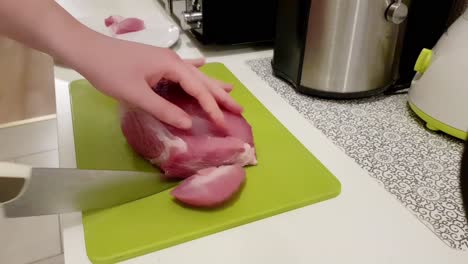 mujer caucásica cortando carne de cerdo con un cuchillo blanco en un tablero verde