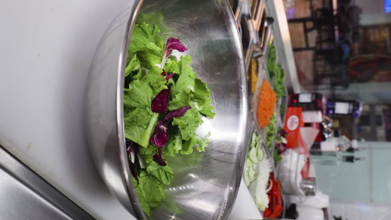 video vertical cercano de un cocinero preparando una ensalada en un cuenco metálico
