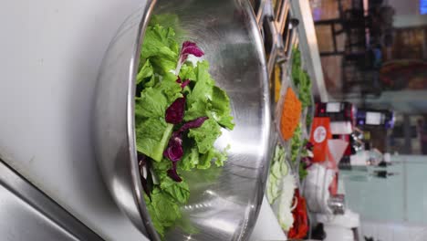 Close-vertical-video-of-a-cook-preparing-a-salad-on-a-metallic-bowl