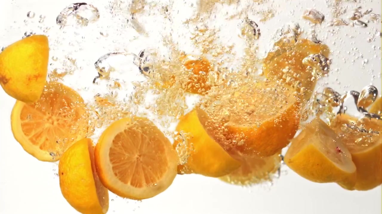 Fresh Lemon Slices and Whole Lemons Splashing into Clear Water in Slow Motion