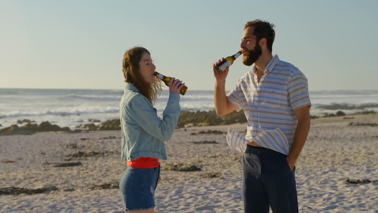 은 날 해변에서 맥주를 마시는 젊은 부부 4k