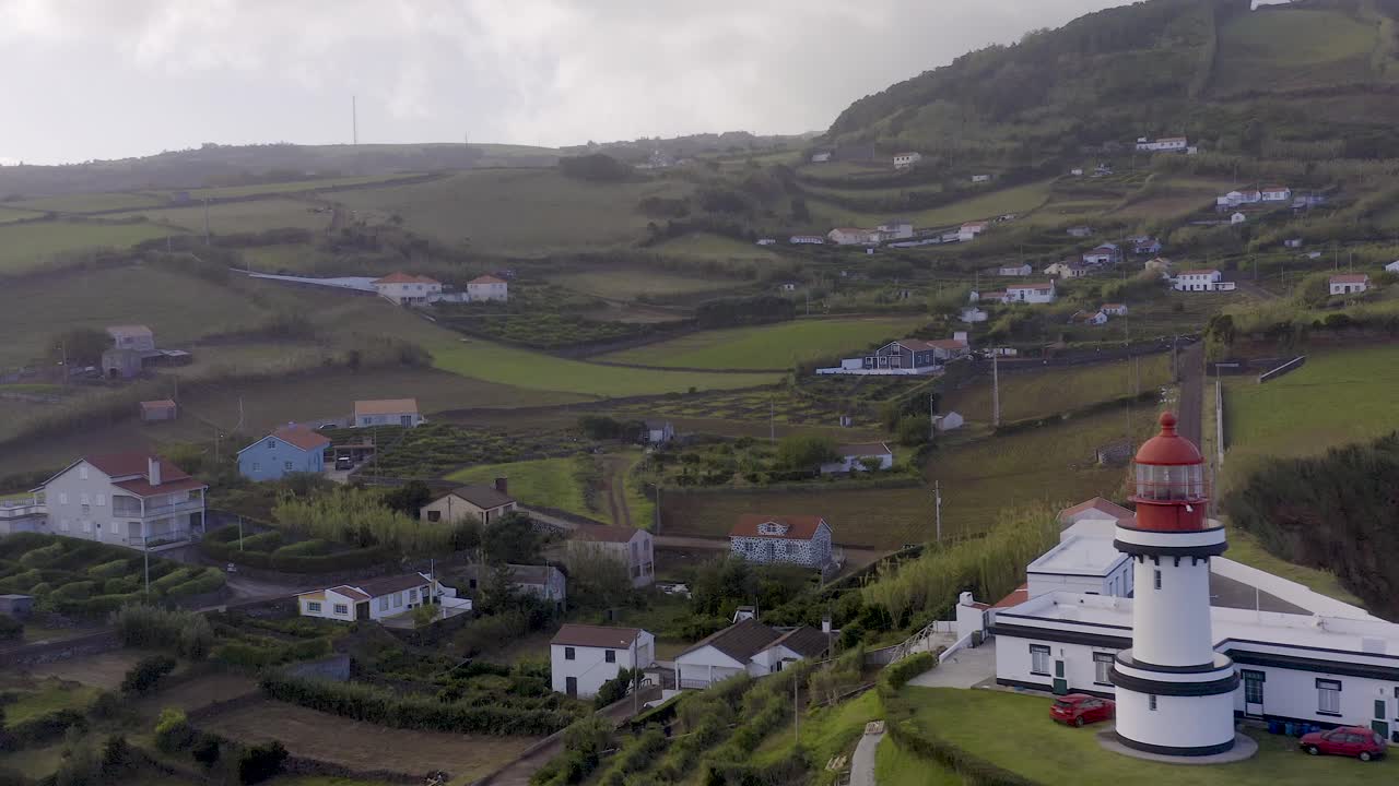 vista de drones de un pueblo con un faro, cielo nublado en topo, isla de são jorge, azores, portugal