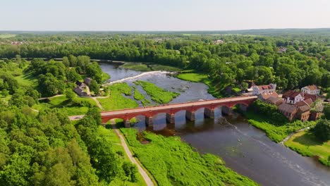 fast drone view of red brick bridge and ventas rumba waterfall in lush valley