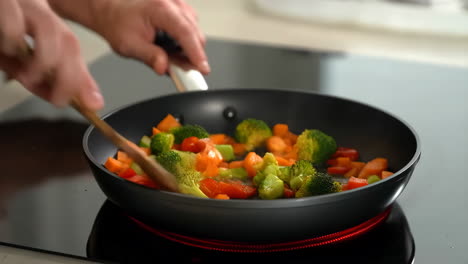 hands stirring chopped vegetables in a frying pan
