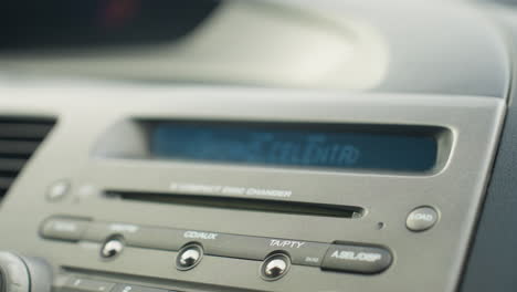 close up of car dashboard displaying built-in cd player with labeled control buttons and digital screen showing music information inside vehicle interior during daylight