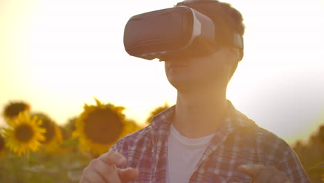 un joven gerente agrícola en camisa a cuadros y vaqueros usa gafas vr en el campo con girasoles para un artículo científico. estas son tecnologías modernas en la noche de verano.