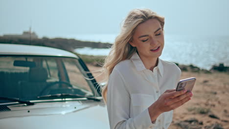 mujer usando el teléfono por un coche de época en la playa