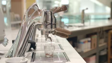 Worker-leaves-stainless-silver-espresso-machine-as-it-drips-coffee-into-single-glass-cup