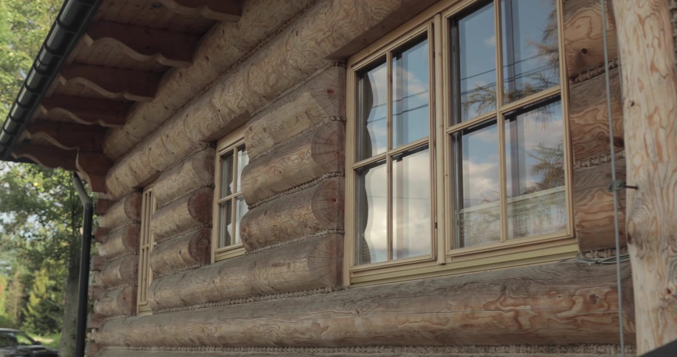 Casa in legno a Zakopane, Polonia, con alberi verdi sullo sfondo e un cielo blu riflesso nelle finestre, ripresa dinamica in 4K.