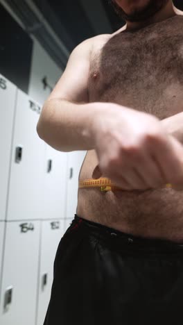 man measuring his waist in a locker room