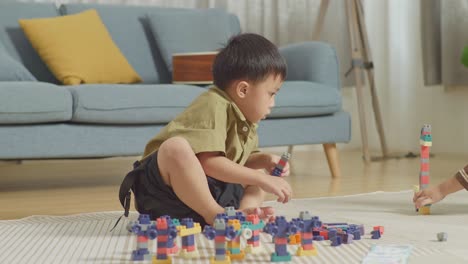 full body of asian kids assemble the construction set colorful plastic toy brick on a mat at home