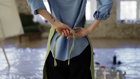 Rare view woman fasten up green apron in art studio