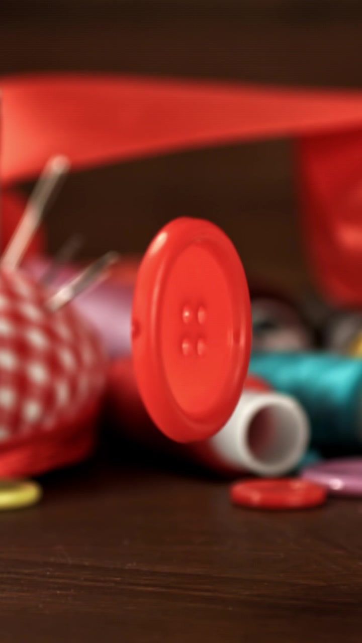 Red Button Falling and Spinning in Slow Motion with Sewing Supplies