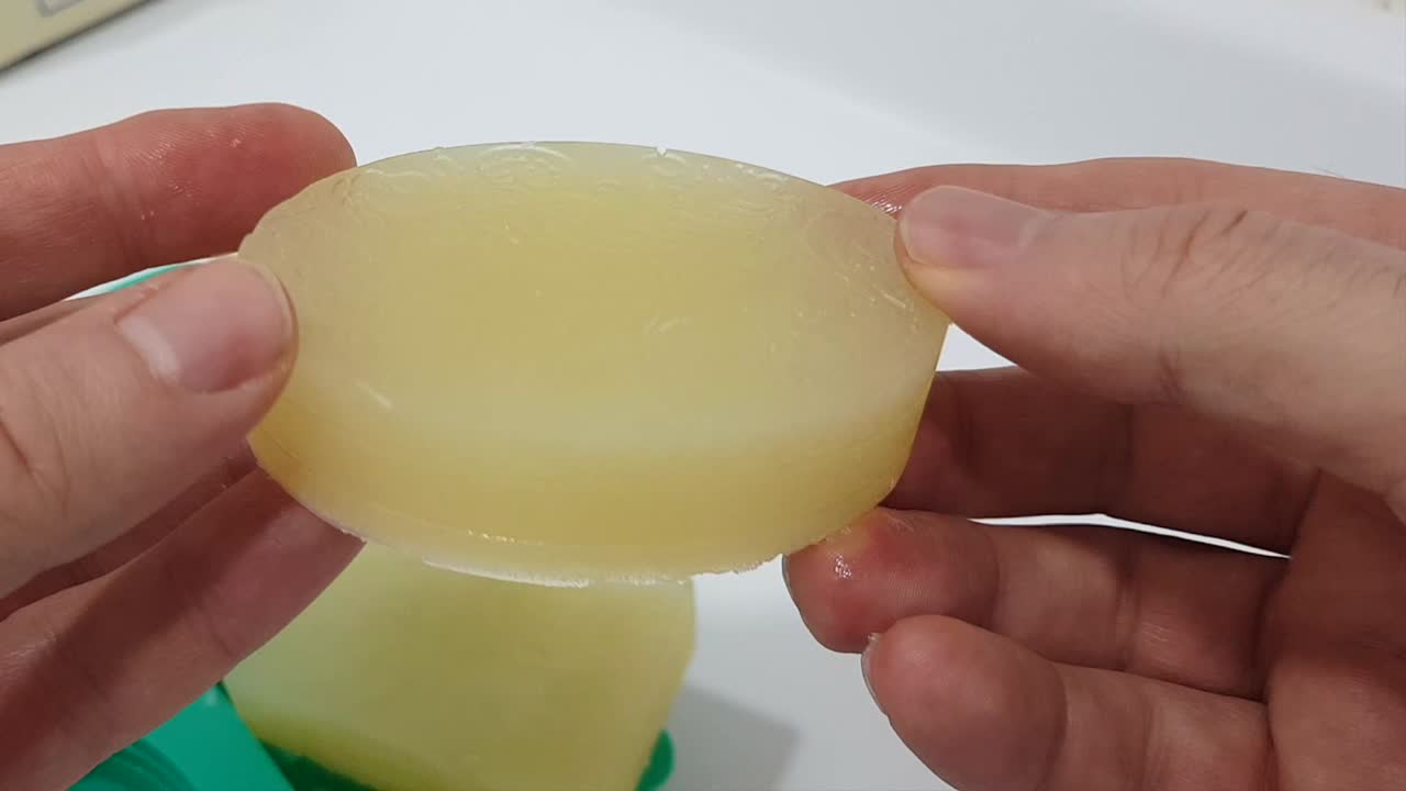 vista de cerca de manos con guantes azules desmoldando barras de jabón recién hechas usando un molde de silicona en un laboratorio de cosméticos naturales.