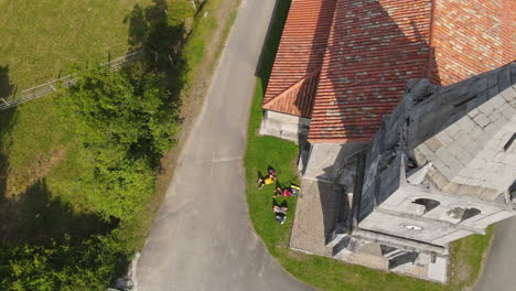 Luftaufnahme-Von-Drei-Rucksacktouristen,-Die-Sich-Auf-Gras-In-Der-Nähe-Einer-Alten-Kirche-Ausruhen