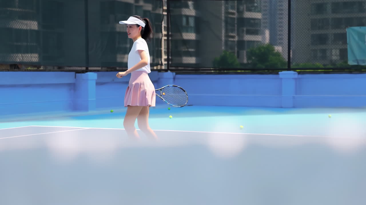スポーツウェア姿の運動能力の高い女子テニス選手が、プロのラケットでテニスボールを真剣に打ち込み、コートでの練習中にボールを打ち続けている。