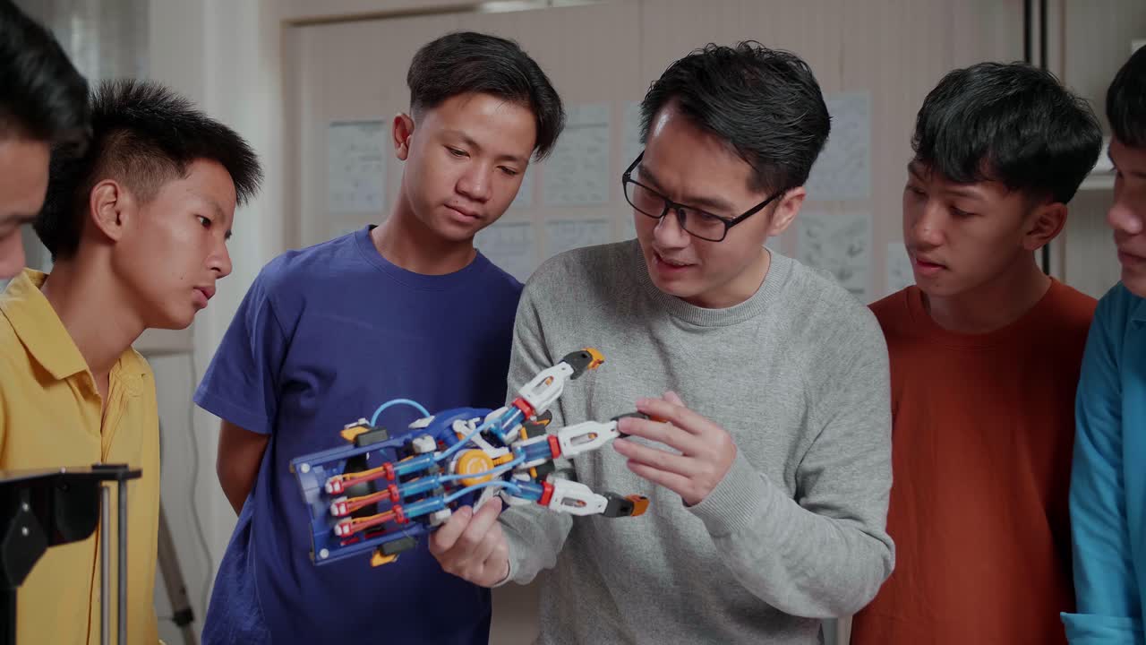 hombre asiático con impresión 3d usando una computadora portátil y explicar acerca de una mano cyborg a los niños en la escuela