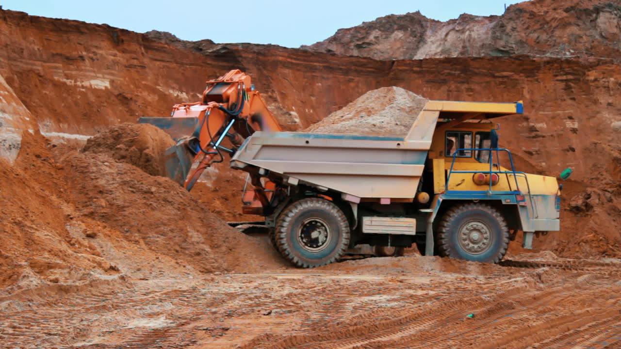 Excavator loading sand into dumper truck. Crawler excavator working
