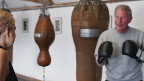 Senior-Male-Boxer-With-Younger-Female-Coach-In-Gym-Using-Training-Gloves