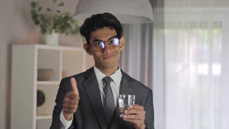 Man-wearing-a-suit-pointing-to-a-glass-and-giving-a-thumbs-up-while-nodding