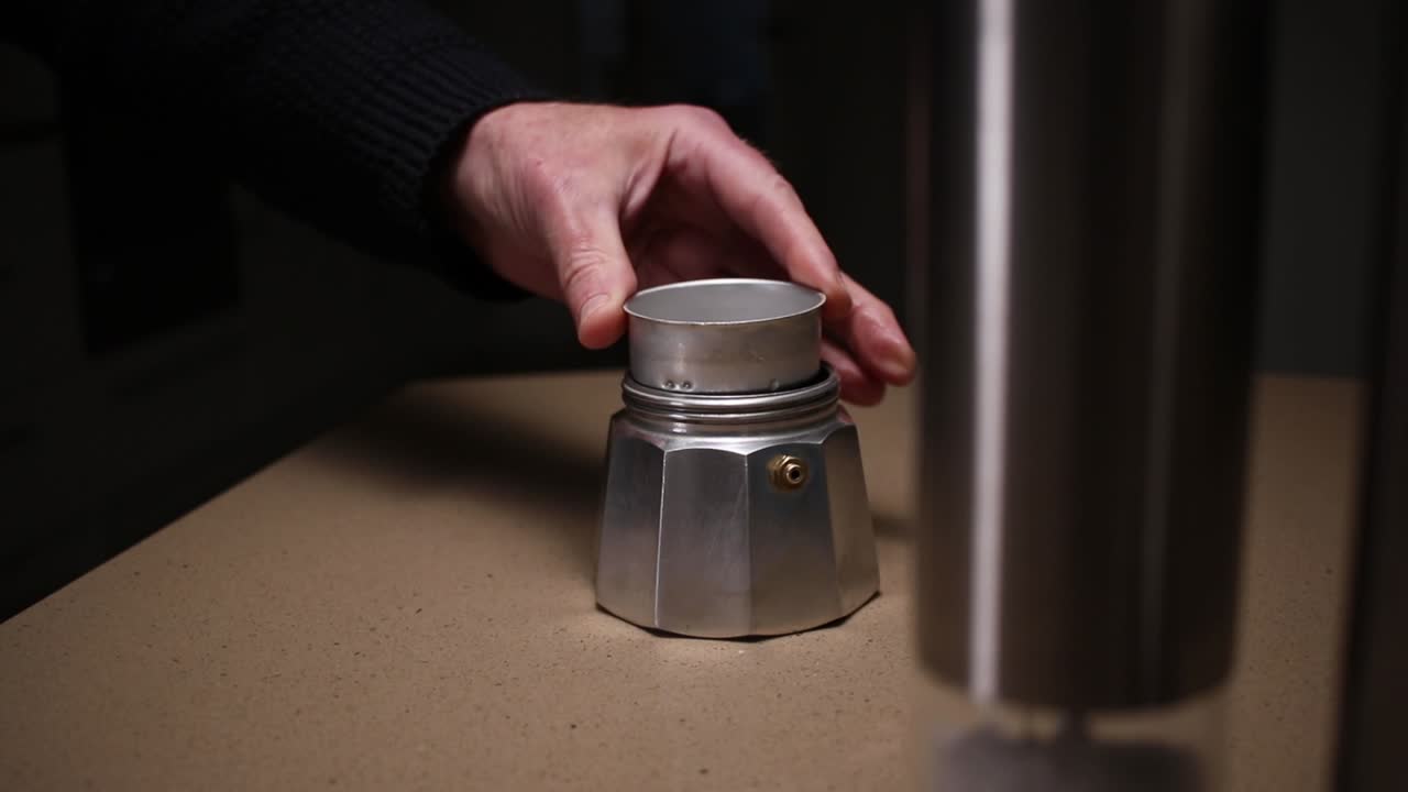 Dolly footage of filter section and ground coffee being placed in the base section of a Moka stove top Italian espresso coffee maker.
