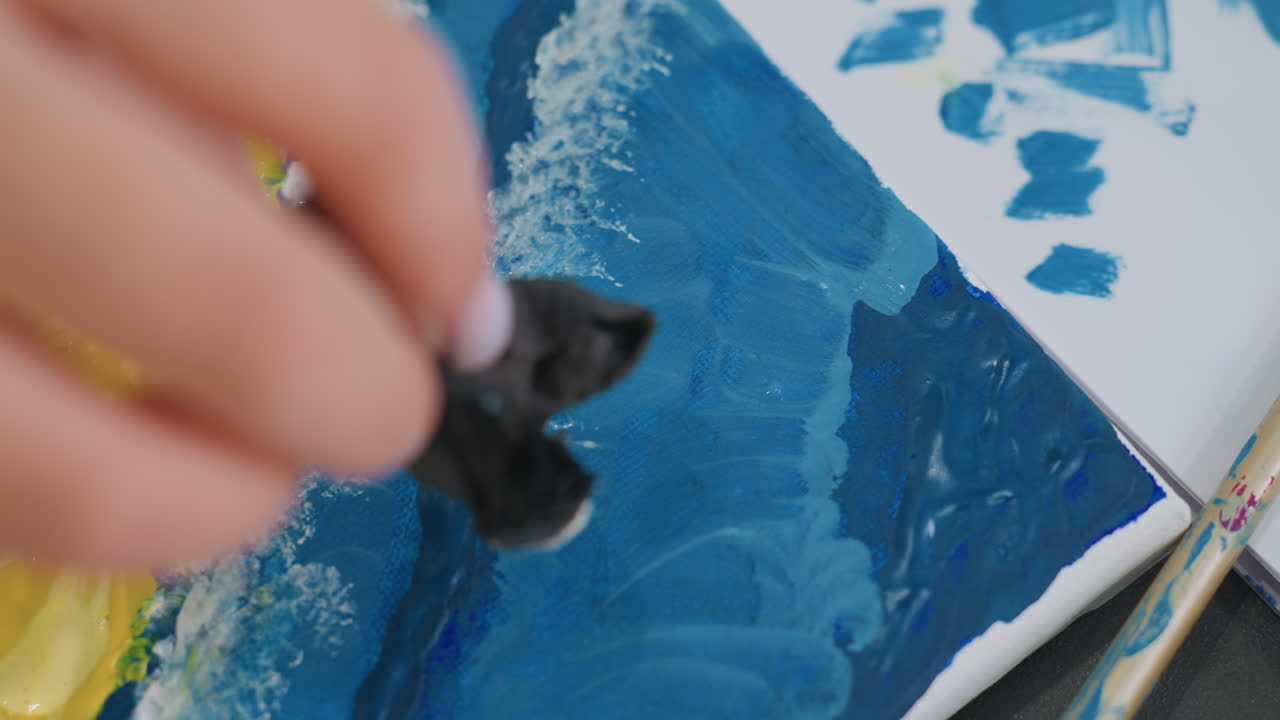 텍스처가 있는 파란색 스트로크로 그림을 그리는 파란색 브러시워크 활동은 스펀지를 사용하여 그림자 효과를 적용합니다. 집중한 화가는 스펀지를 짙은 파란색으로 눌러 파도 그림자를 생생하게 만듭니다.