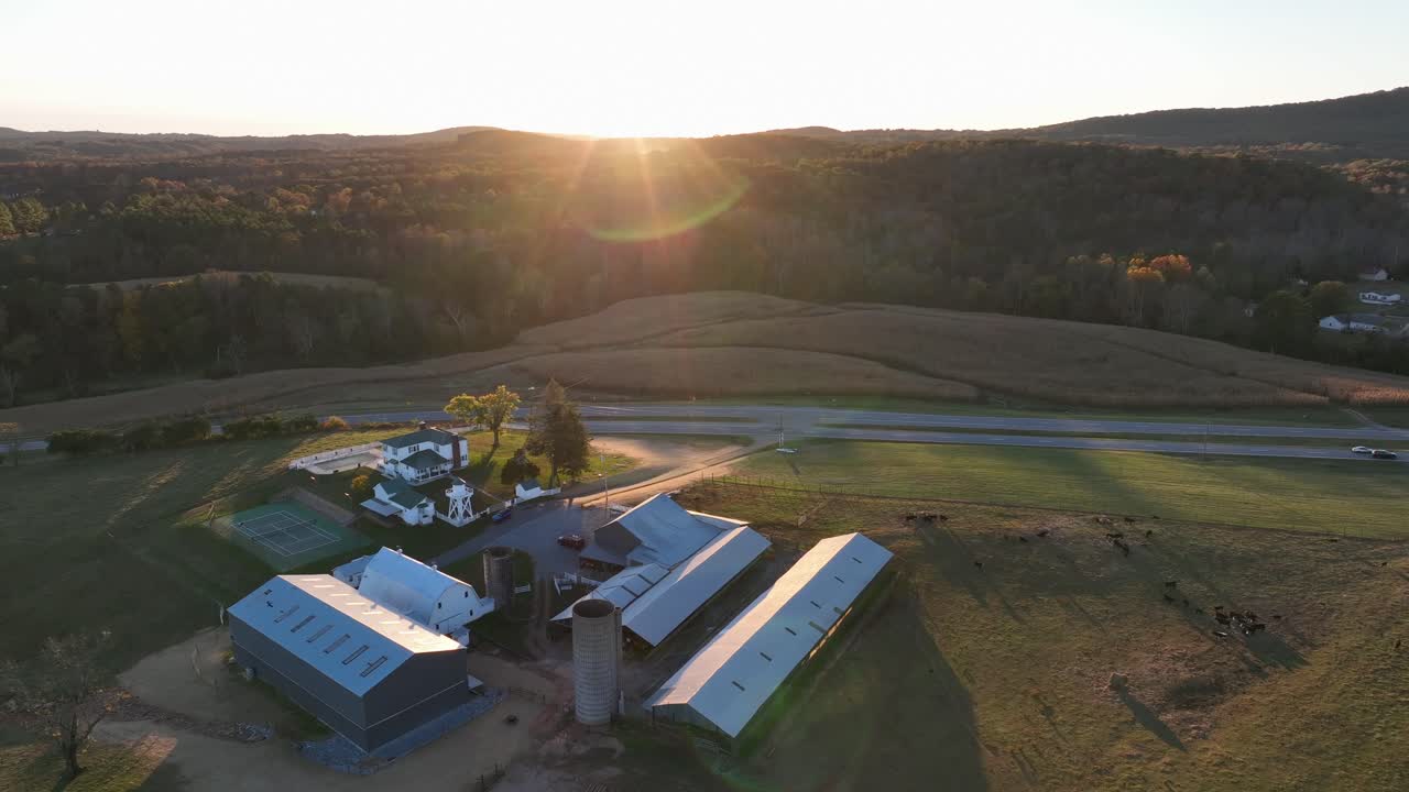 Aerial rising shot of american farmstead with barn and buildings in USA. Sunset light behind green mountains of Lynchburg, Virginia. Rural area of american town with road