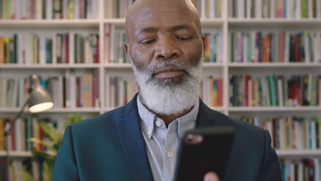 close up portrait of mature african american businessman boss looking serious texting browsing using smartphone mobile networking app in library bookshelf background