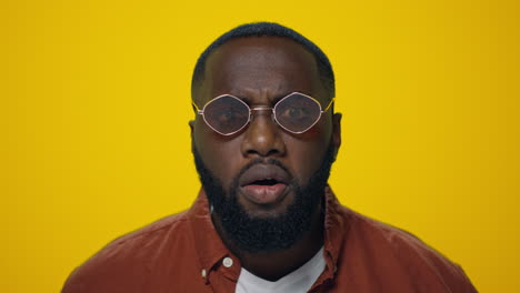 retrato de un hombre africano enojado gritando con gafas de sol sobre un fondo amarillo.