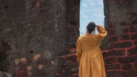 Woman-in-yellow-dress-gazing-through-ruins-at-the-sky-on-a-sunny-day