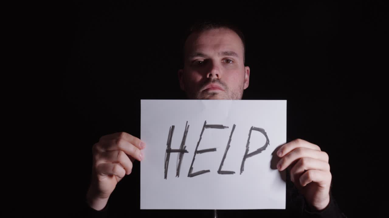 Man walking toward camera holding a “help” sign, symbolizing reaching out, mental health awareness, and need for support