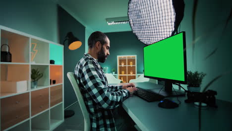 joven autónomo, redactor, diseñador, editor o creador de contenido que trabaja en una computadora de escritorio con una pantalla verde de croma clave simulada