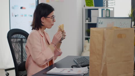 mujer de negocios comiendo un bocado de sándwich sabroso bebiendo café frente al monitor