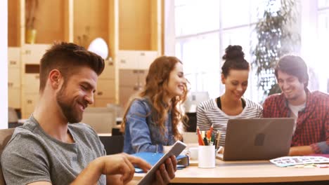 Male-business-executive-using-digital-tablet-while-colleagues-interacting-at-desk