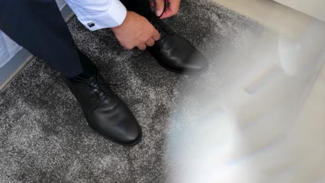 business man tying shoe laces on the floor groom is wearing black shoes in close