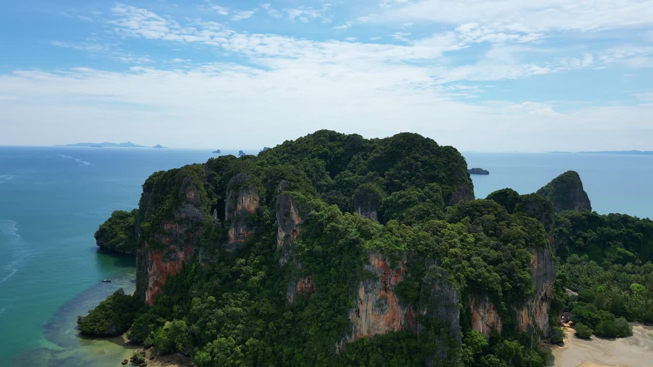 Veduta aerea di un'isola verde lussureggiante con scogliere a picco, circondata da acque blu tranquille sotto un cielo luminoso.