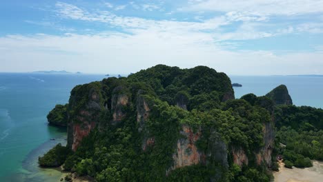 aerial view of a lush green island with steep cliffs surrounded by tranquil blue waters under a bright sky.