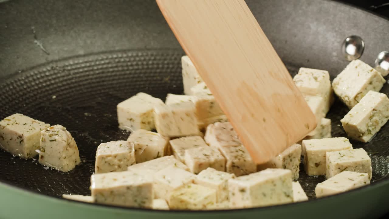 Fried tofu with sesame seeds and spices on cast iron pan, cooking japanese salad. Healthy ingredient for cooking vegan vegetarian diet food. Roasted tofu over black background.