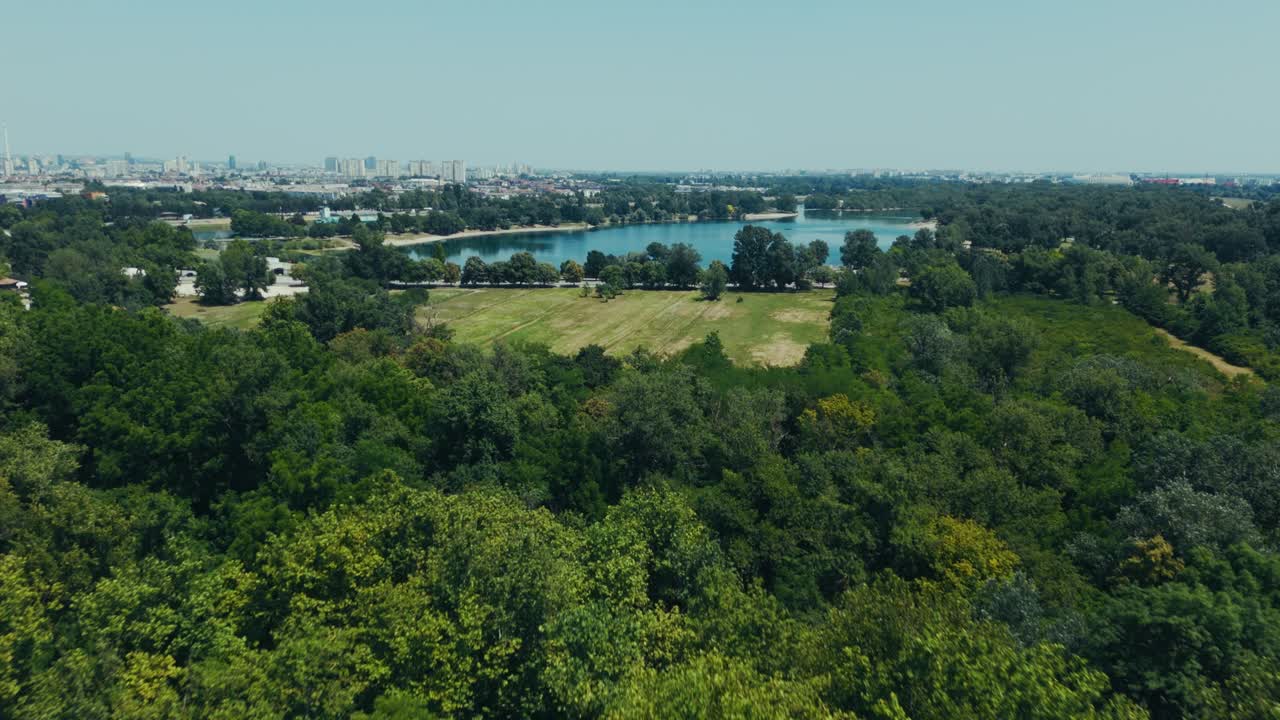 aerial wide of green forest with lake Jarun and Zagreb city skyline in summer light