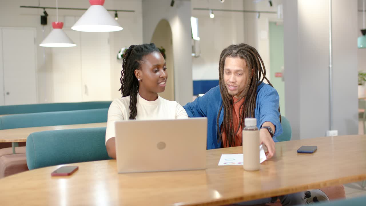 Colleagues reviewing content at long wooden table, woman operating laptop while man pointing paper