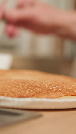 female hand in white shawl applies spread on pastry with silicone brush. process of making delicious cake in home kitchen on blurred background closeup