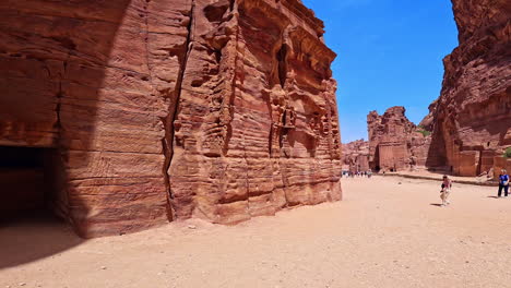 stone-cut facades of ancient petra, jordan, west asia. low angle view at the stunning rocks in famous landmark. tourists walk by the area.