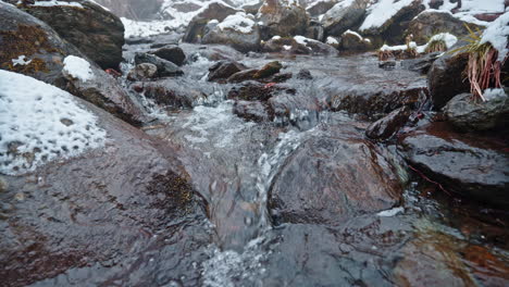 Snowy-mountain-stream-flows-over-rocks-in-serene-winter-landscape,-close-up