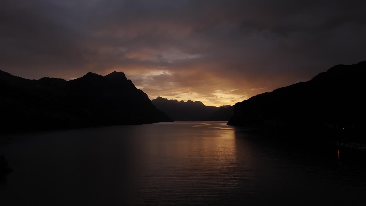 Sunset over Walensee with mountains silhouetted against the glowing sky and calm waters below