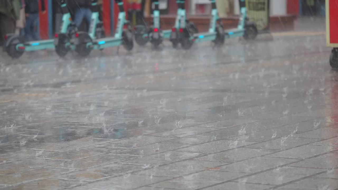 背景に電動スクーターがある市街地の舗道に降る激しい雨
