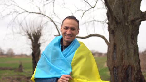 el ganador de la silueta exitosa ondeando la bandera ucraniana cerca de un árbol quemado
