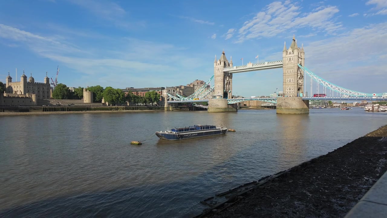 Il Tower Bridge attraversa il fiume Tamigi a Londra mentre le oche si radunano sulla riva del fiume sotto cieli diurni luminosi.