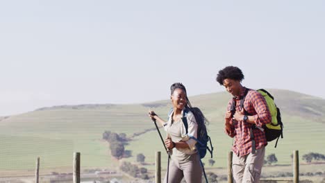 Happy-african-american-couple-with-backpacks,-hiking-with-trekking-poles-together,-slow-motion